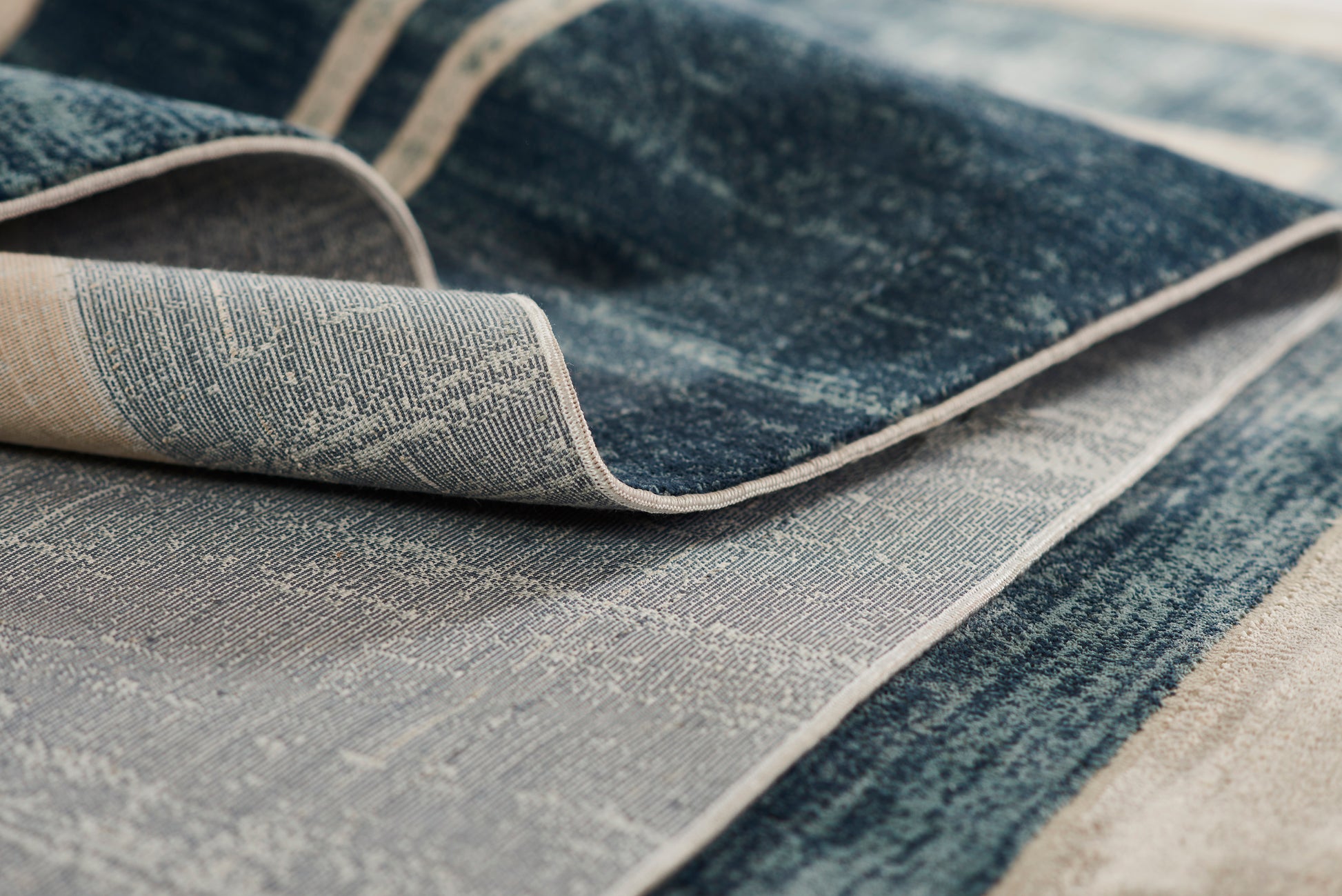 Blue denim-style rug with beige trim, textured weave, folded edges for casual decor.