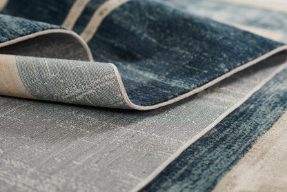 Close-up of a blue and cream woven rug with denim-like tones and beige edge, folded corner.