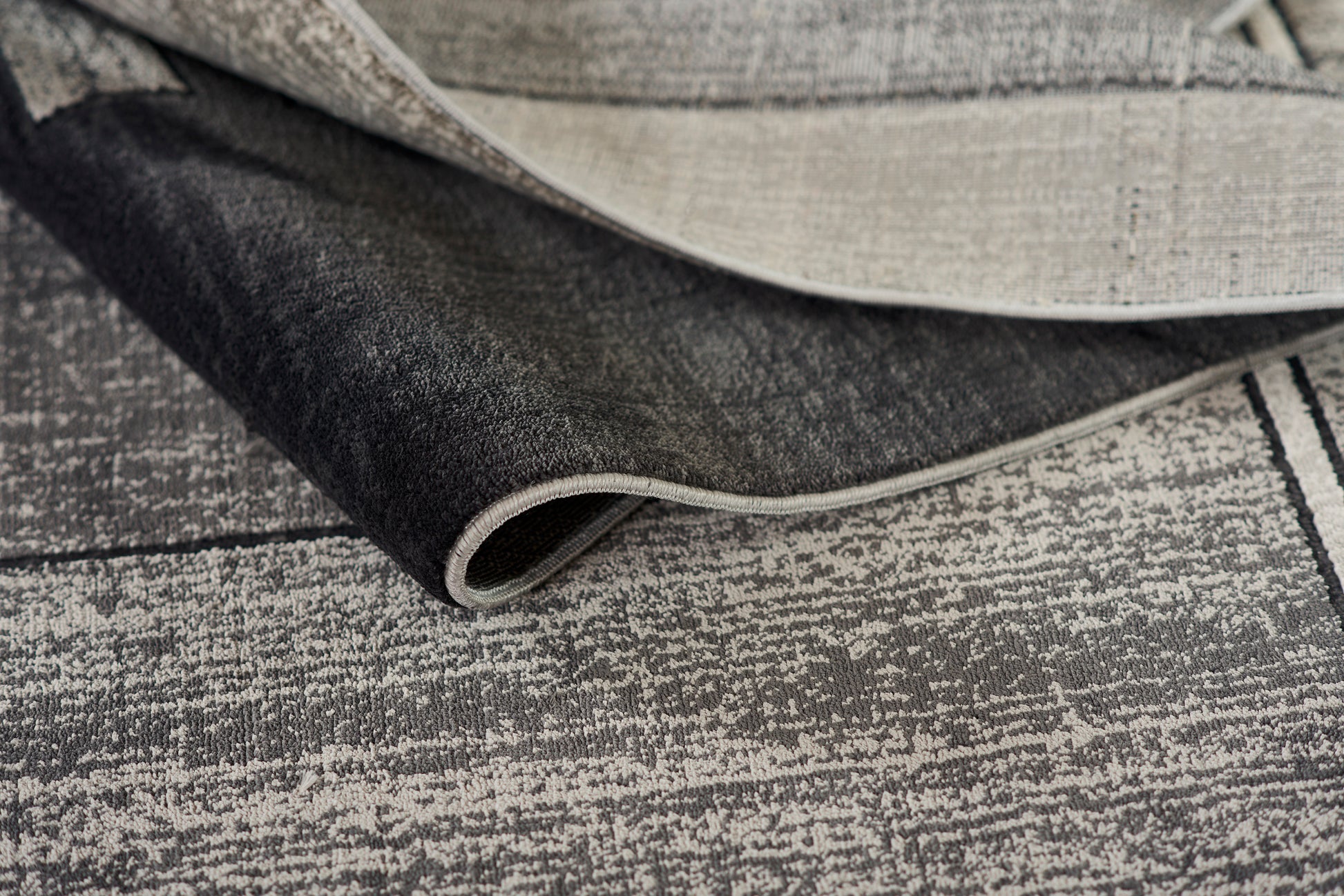Two-tone woven rug in dark charcoal and beige with a textured weave.