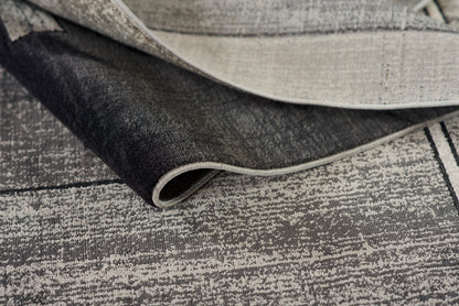 Neutral gray and beige woven rug with a distressed linear pattern; rolled corner reveals soft textile.