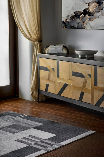 Geometric wood sideboard with black frame and warm panels; beige drapes, abstract marble art, books and bowl atop; grey rug.