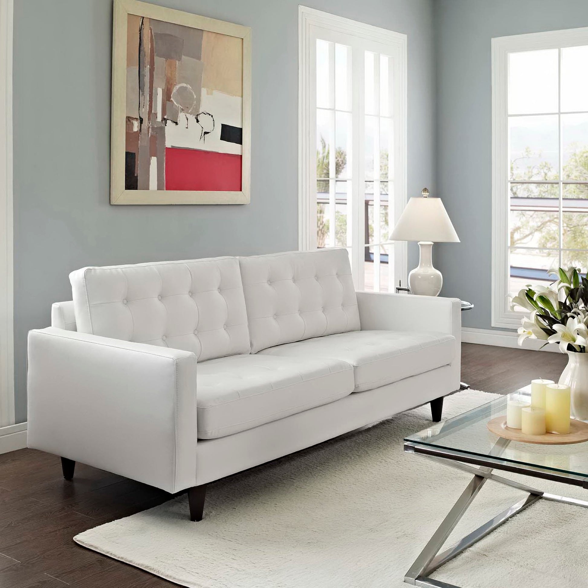 White tufted sofa with dark wood legs in a bright living room featuring a glass coffee table and abstract wall art.