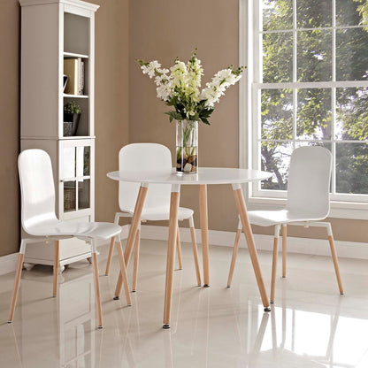 White round dining table with light wood legs, three white chairs, a vase of white flowers, in a sunlit dining room.