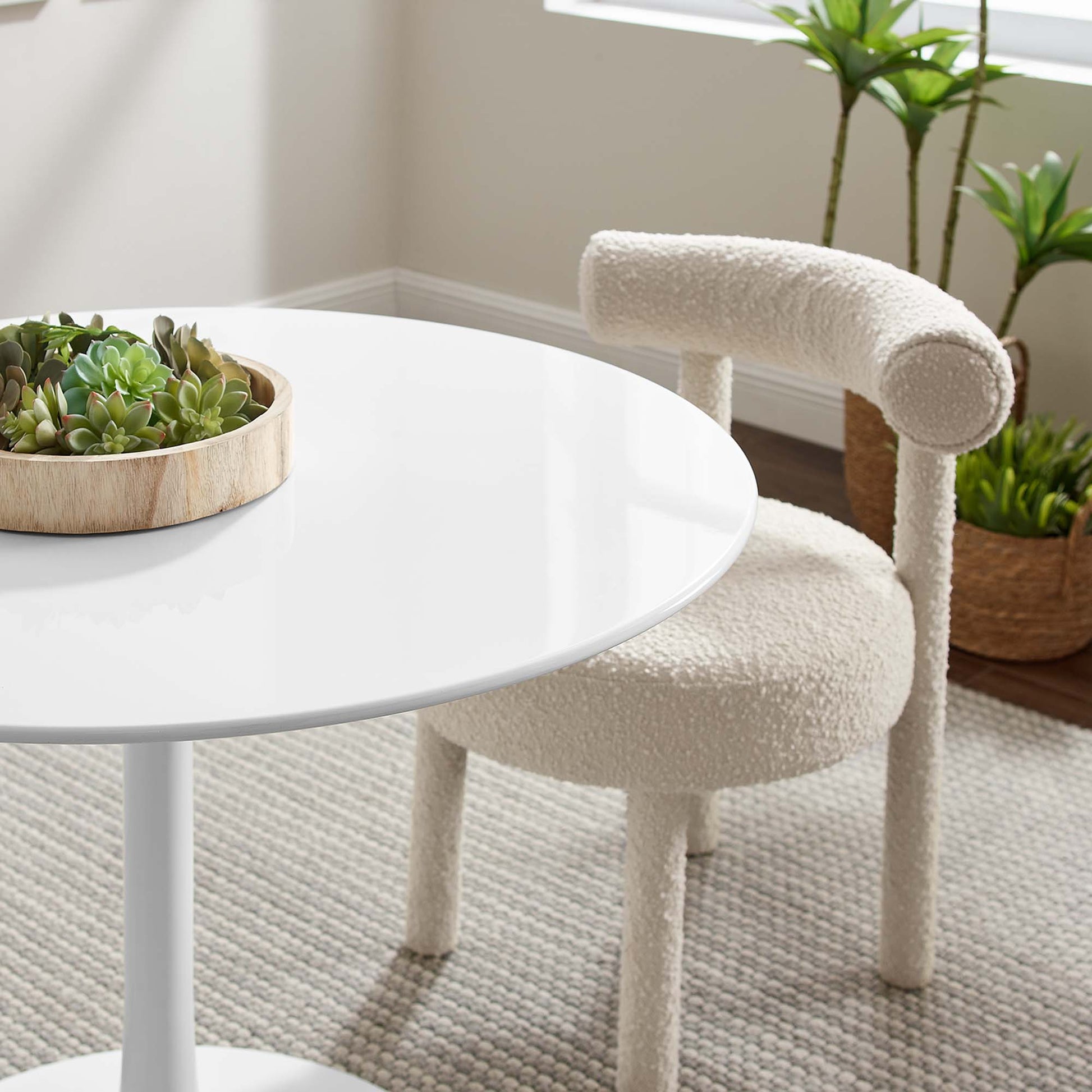 White round table with glossy surface; cream boucle chair; wooden tray of succulents and potted plants.