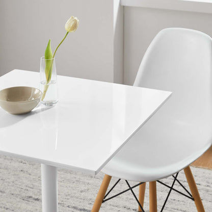 White glossy square dining table with a glass vase holding a white tulip and beige bowl; molded chair with wooden legs.