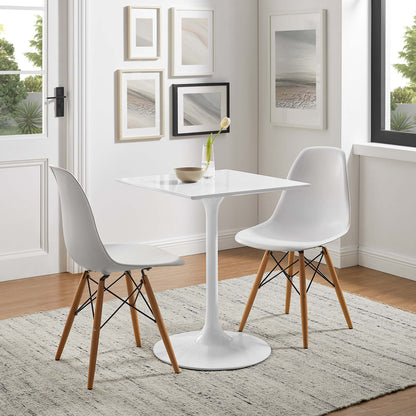 White tulip pedestal dining table with square top, flanked by white mid-century molded-shell chairs with wooden legs.