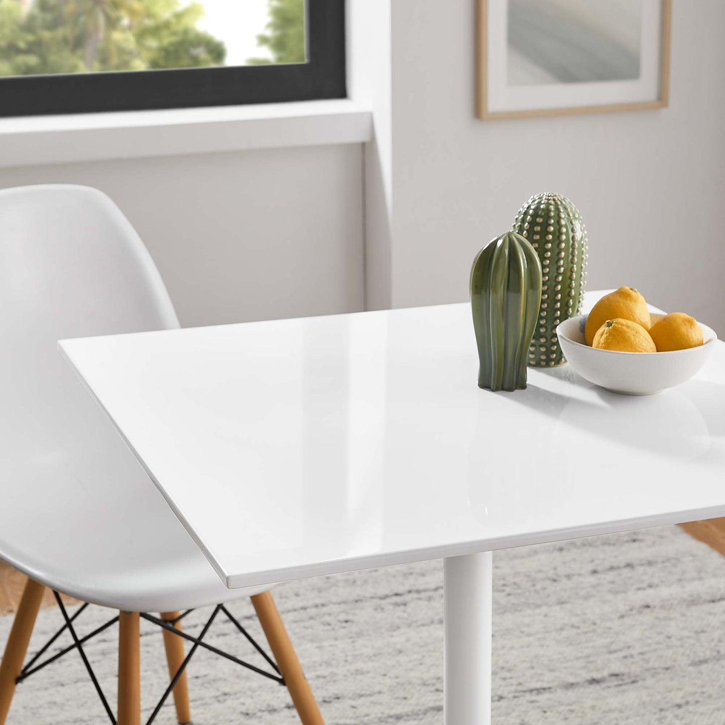 Glossy white rectangular dining table with white molded chair, cactus decor and a bowl of lemons.