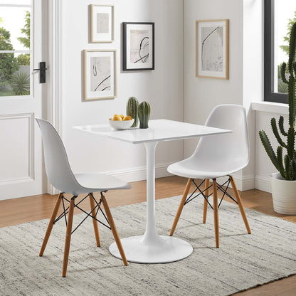 White tulip-pedestal dining table with square top, white molded chairs with wooden legs, fruit bowl and cactus, framed art.
