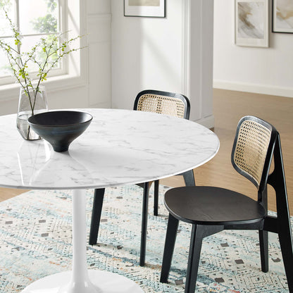Round marble-top dining table with white pedestal base, black chairs with caned backs; modern dining set with vase and bowl.
