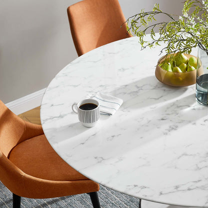 Round white marble table with orange mid-century chairs, coffee mug, bowl of green apples, and leafy centerpiece.
