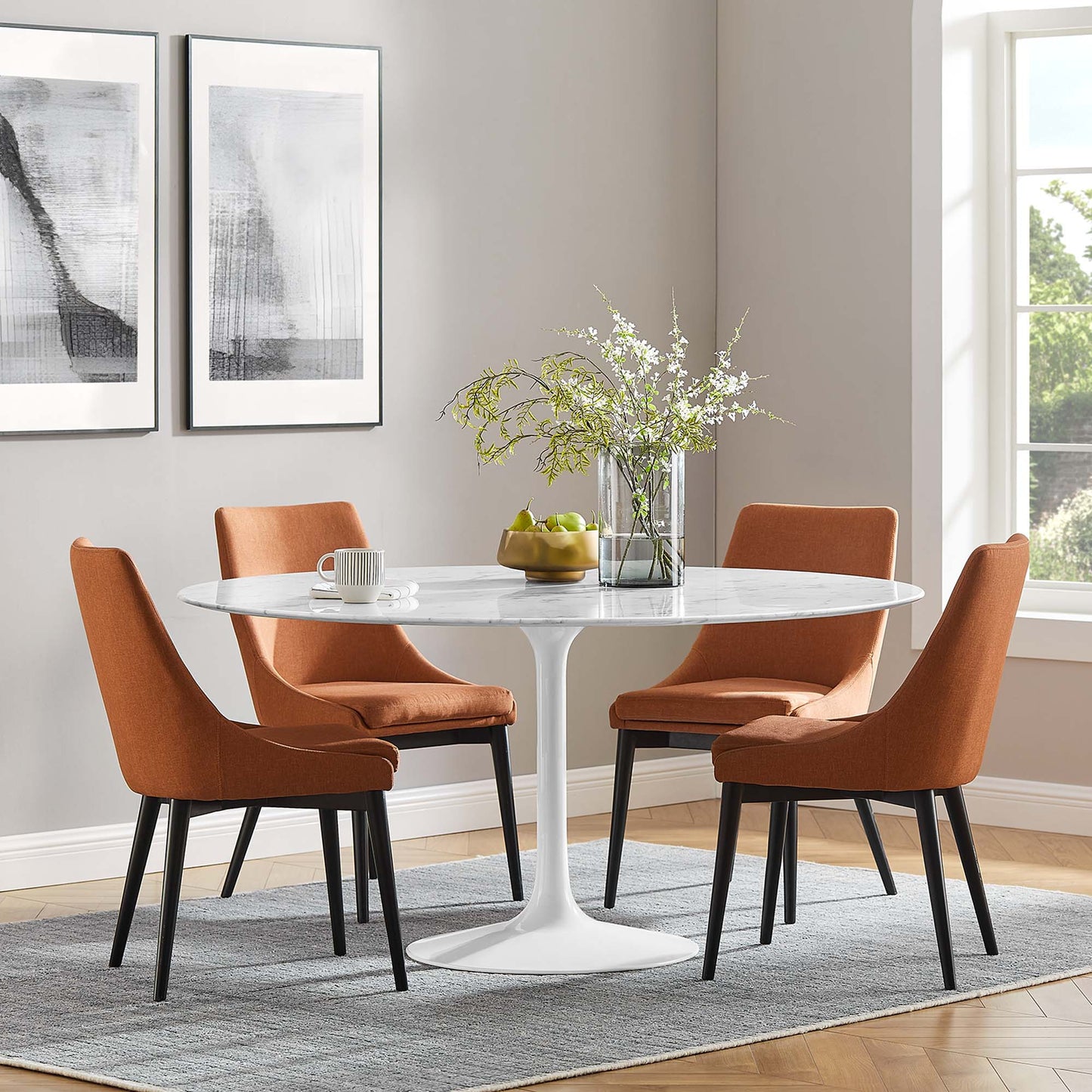 Round white tulip dining table with orange upholstered chairs on black legs, modern dining set on a gray rug.