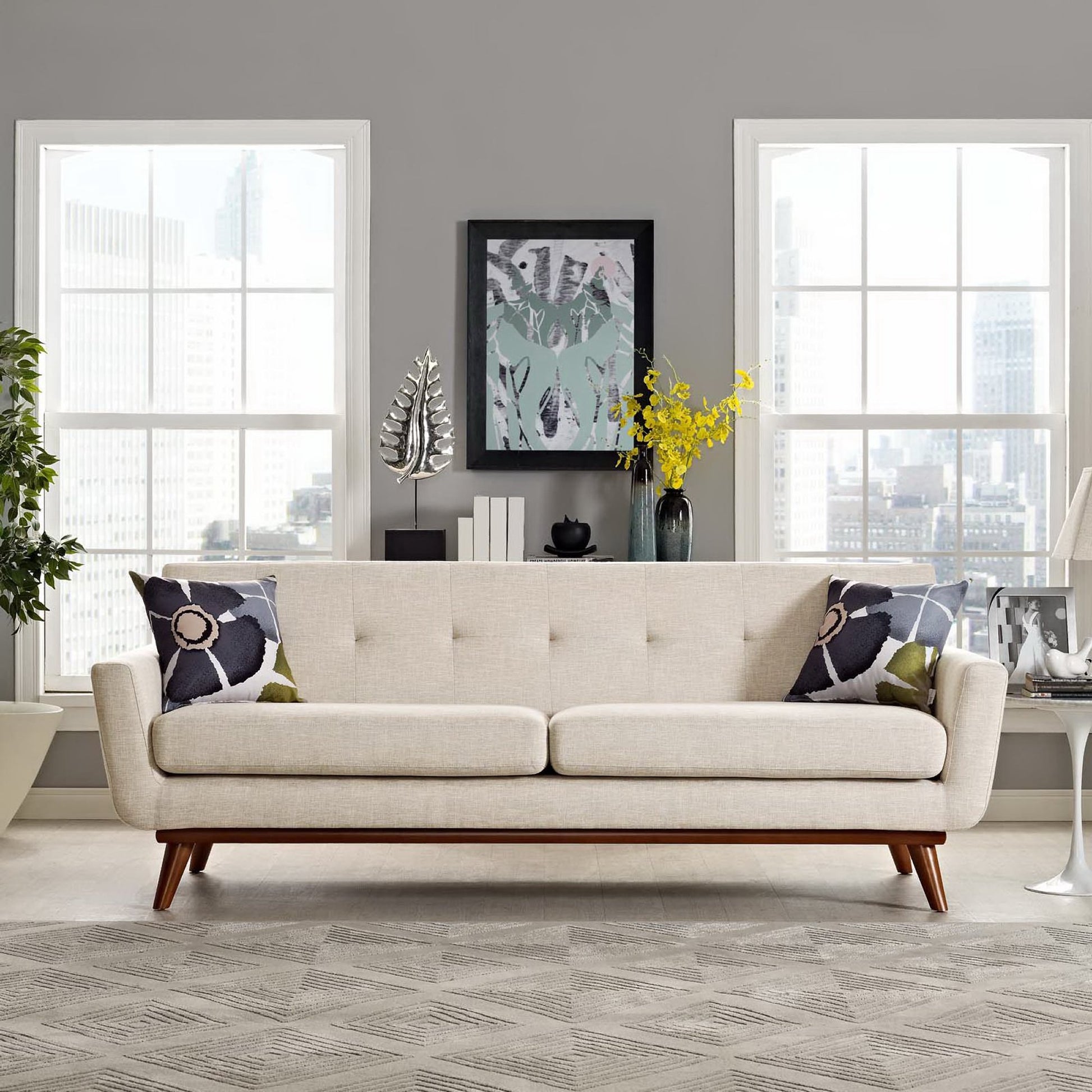 Beige mid-century sofa with tufted back and wooden legs in a gray-walled living room with floral throw pillows.