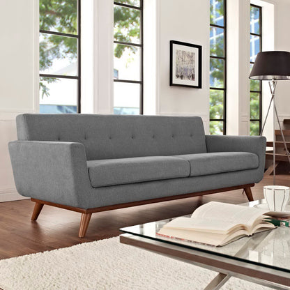 Grey mid-century sofa with tufted back, two cushions and angled wooden legs in a bright living room with large windows.