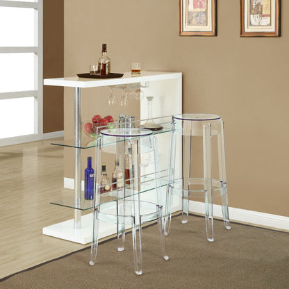Clear acrylic bar stools with rounded seats beside a white bar cabinet with glass shelves and chrome supports.