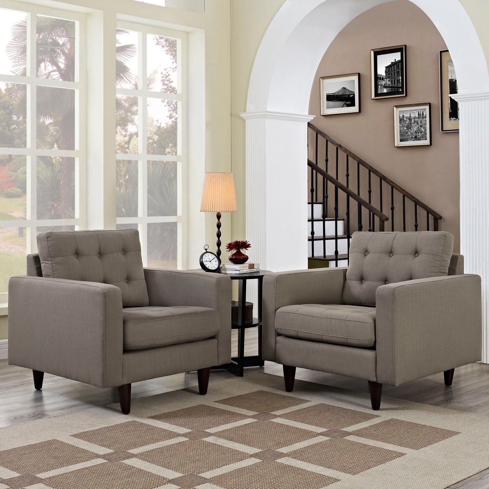Two gray tufted armchairs with dark wood legs around a small round side table with lamp; bright living room, arched doorway.