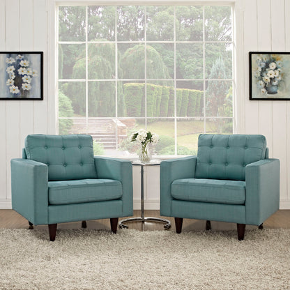 Two teal tufted armchairs with dark wooden legs flank a round glass coffee table in a bright, airy living room.