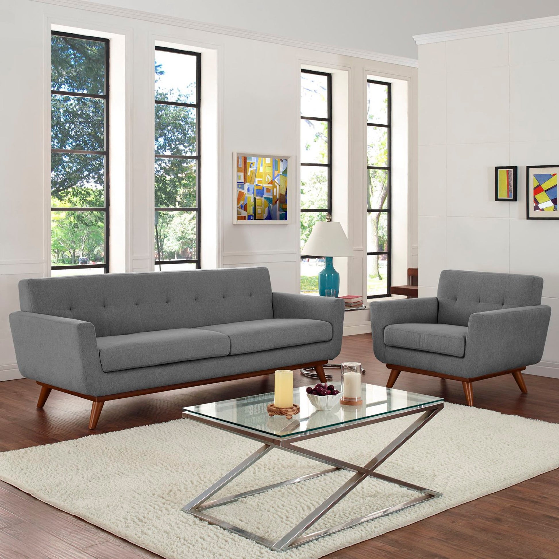 Gray mid-century sofa and armchair with wood legs in a bright living room, glass coffee table with metal X-base