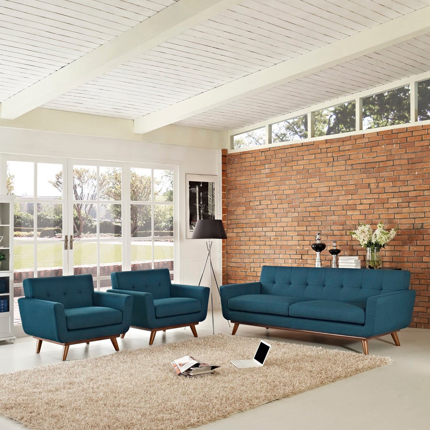 Teal mid-century fabric sofa set with two armchairs, wooden legs, brick wall, beige shag rug, floor lamp.