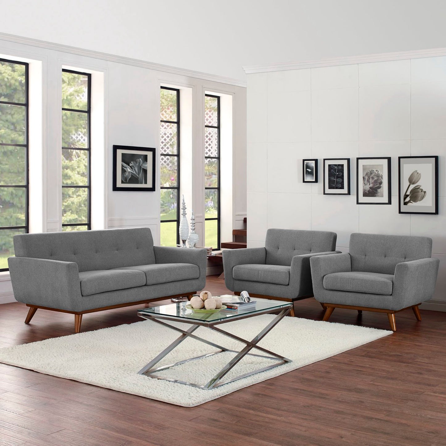 Grey fabric mid-century modern sofa and chairs with a glass-top metal coffee table on a cream rug in a bright living room.