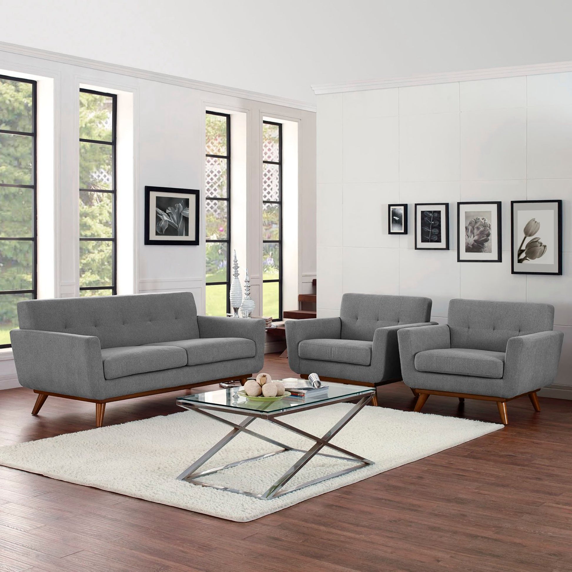 Grey fabric mid-century modern sofa and chairs with a glass-top metal coffee table on a cream rug in a bright living room.