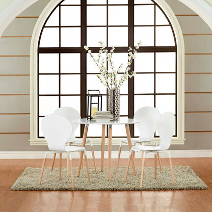 White round dining table with light wood legs and six white molded chairs, vase centerpiece on a rug beside an arched window.
