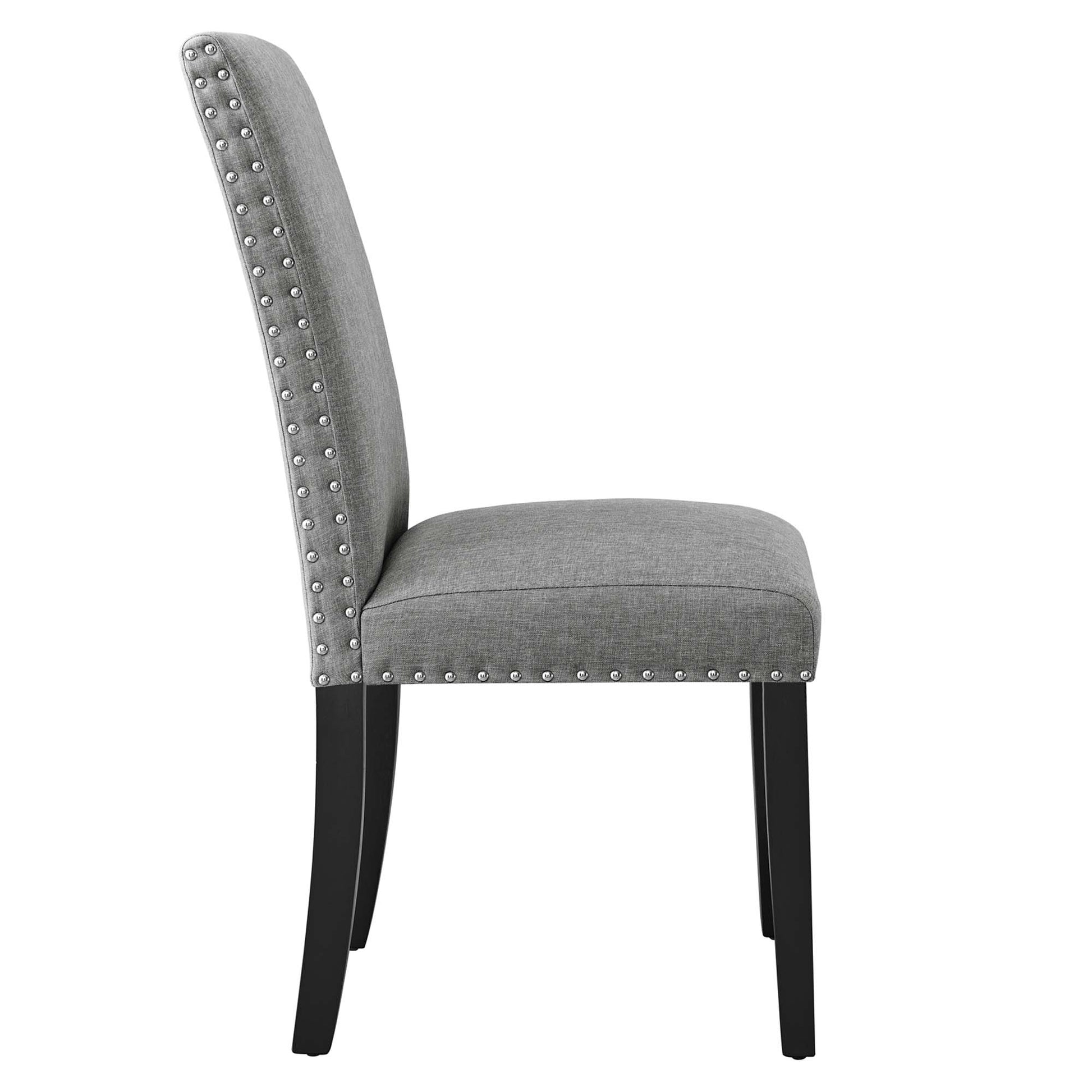 Grey fabric dining chair with nailhead trim along edges, curved back, cushioned seat, black tapered legs.