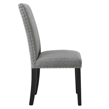 Grey fabric dining chair with nailhead trim along edges, curved back, cushioned seat, black tapered legs.