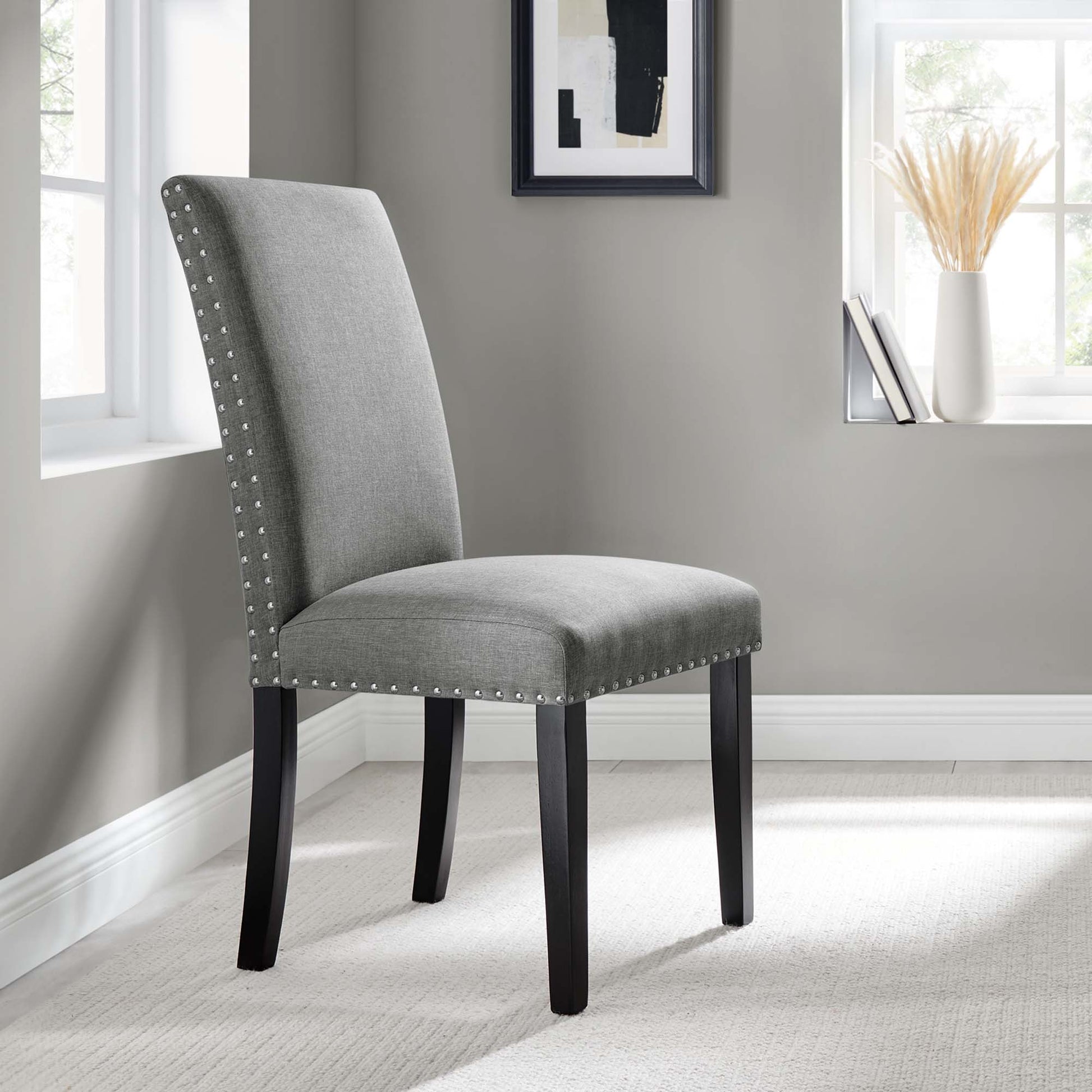 Grey upholstered dining chair with tall back, nailhead trim, and dark curved wood legs.