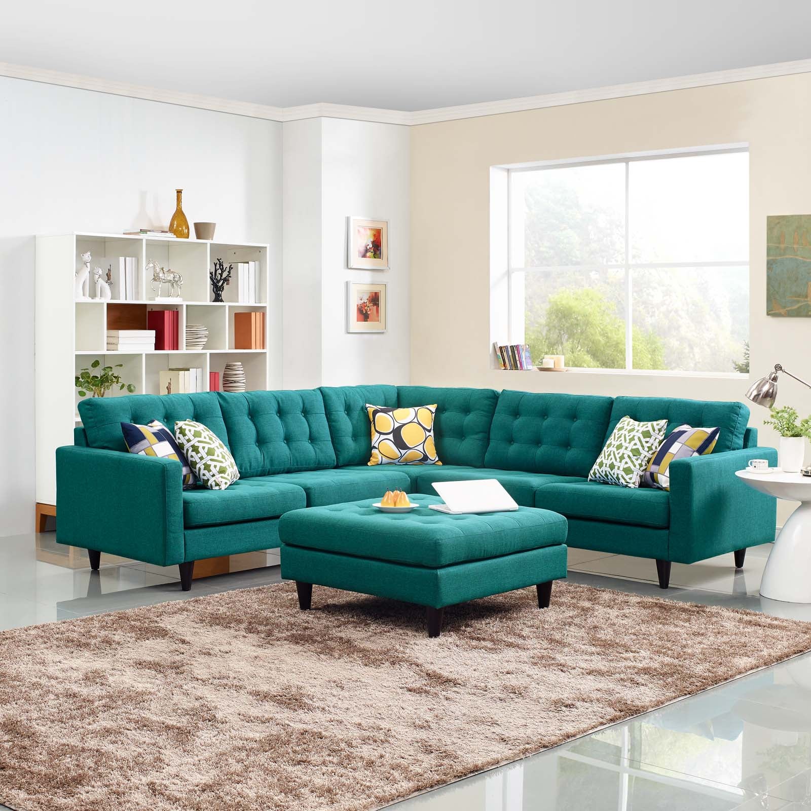 Teal 3-piece upholstered fabric sectional sofa set with matching ottoman in a bright living room, beige rug and white shelving.
