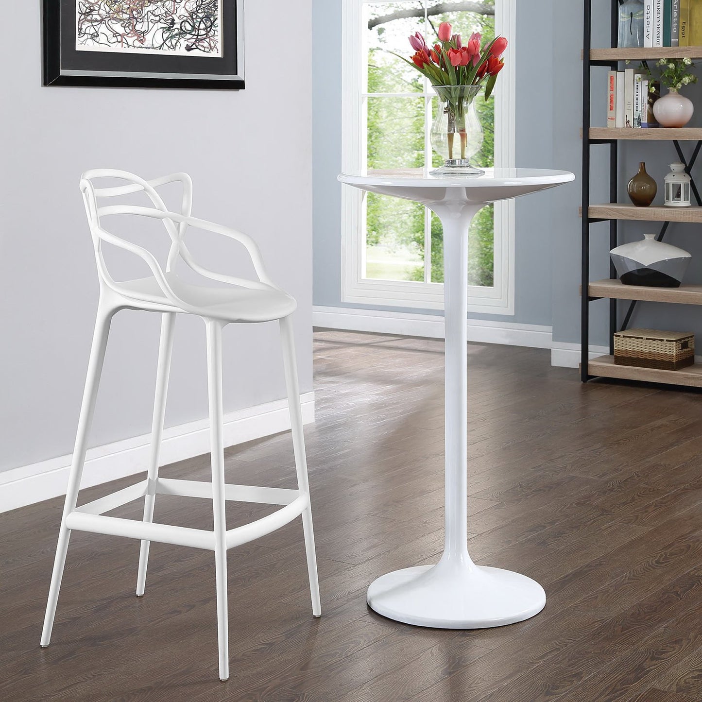 White metal bar stool with curved back beside a round white pedestal table with red tulips, in a bright modern room.