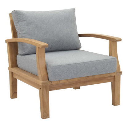 Natural wood outdoor chair with light gray cushions, curved arms and sturdy square legs.