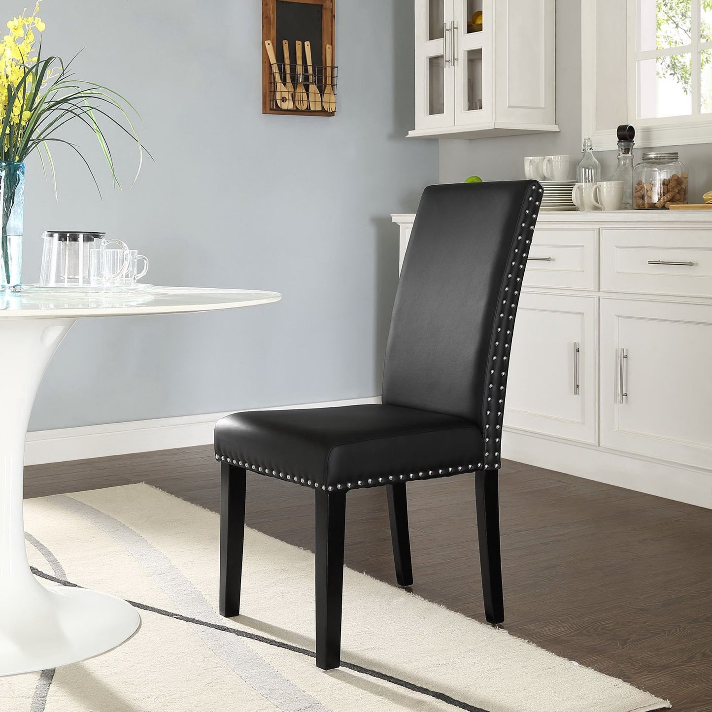 Black faux leather dining chair with nailhead trim and straight back, wooden legs, in a bright kitchen setting.