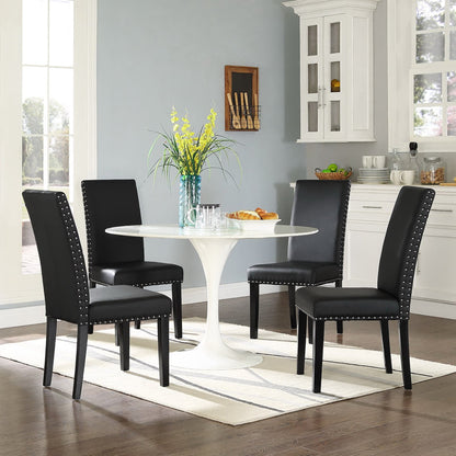 Round white tulip pedestal dining table with four black upholstered chairs with nailhead trim in a bright kitchen nook.