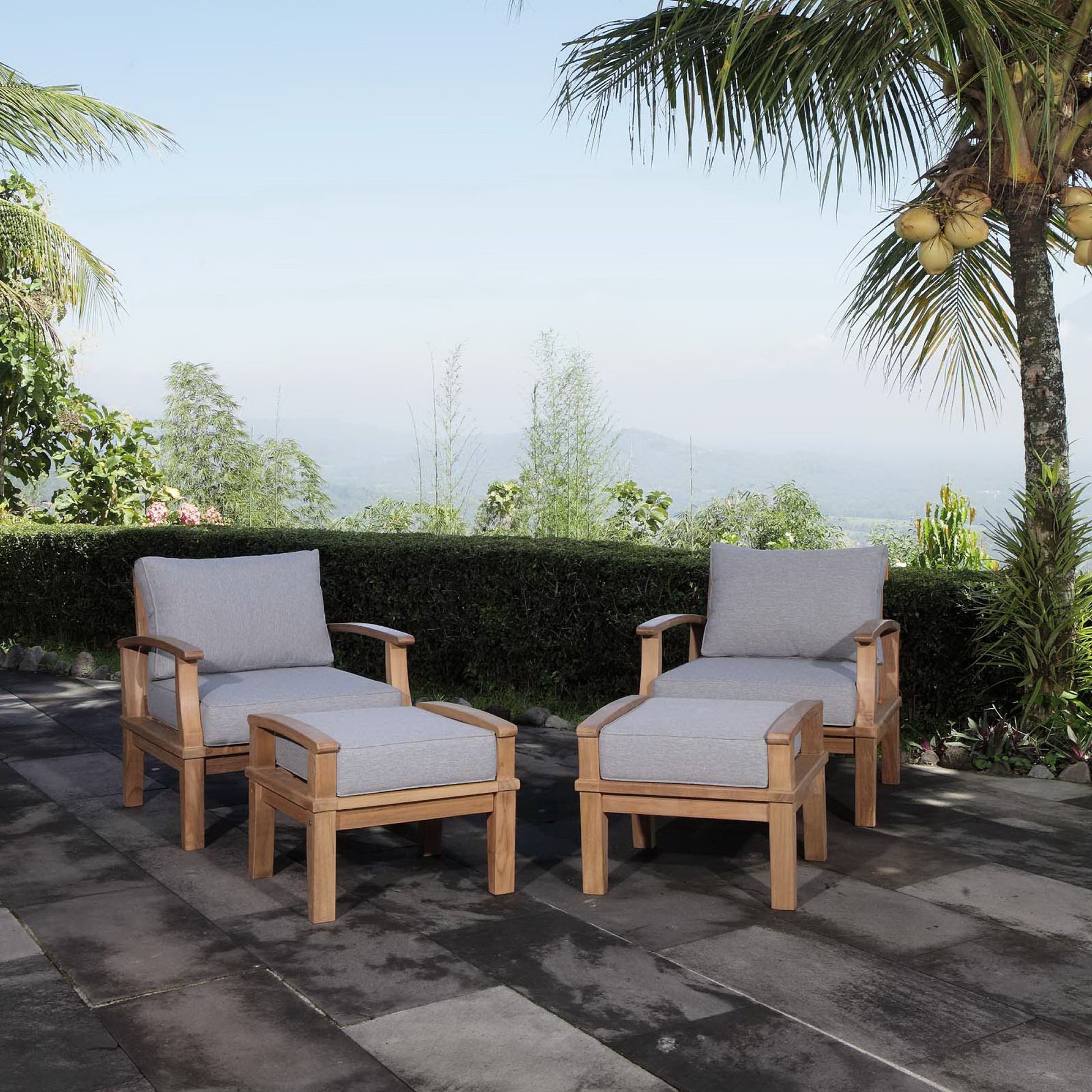 Natural wood outdoor lounge set with light gray cushions: two armchairs and matching ottomans on a stone patio.
