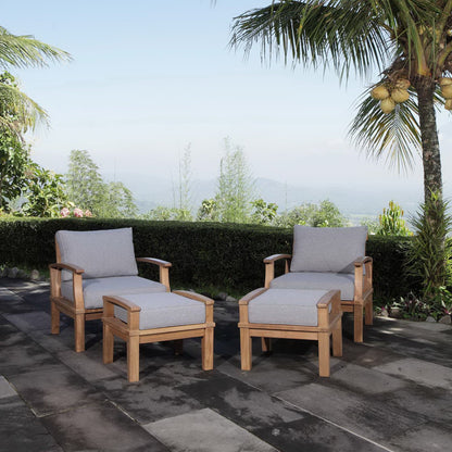 Natural wood outdoor lounge set with light gray cushions: two armchairs and matching ottomans on a stone patio.