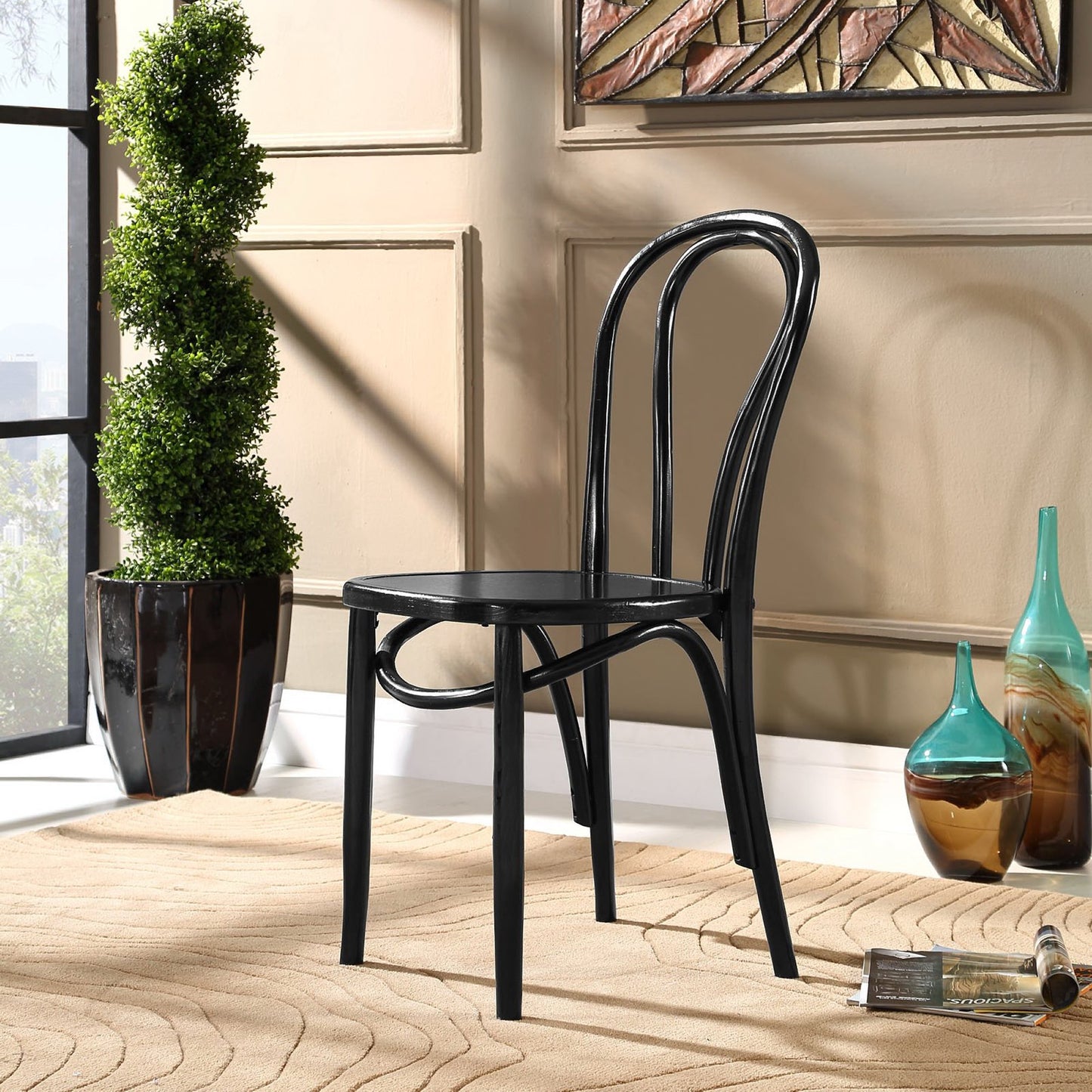 Black bentwood cafe chair with curved back in a beige-walled room on a woven rug beside a green topiary & glass vases.
