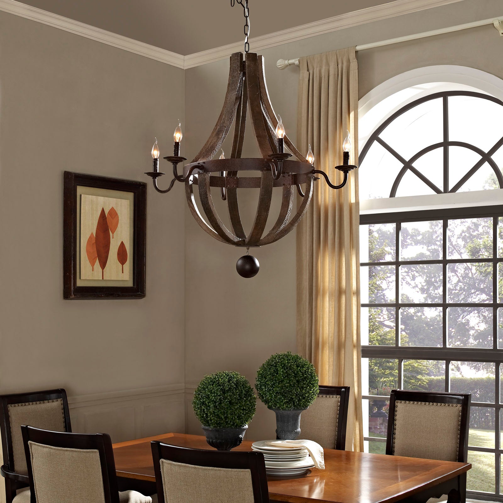 Antique-brass spherical chandelier with candles above a wooden dining table; topiary centerpieces and beige chairs.