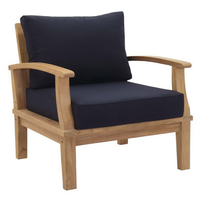 Natural wood outdoor armchair with navy cushions; curved arms, sturdy square legs, cushioned seat & back.