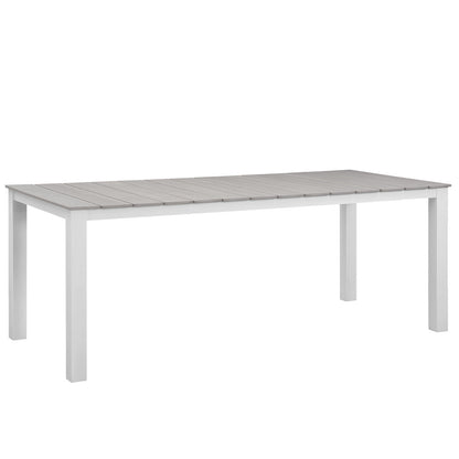 Rectangular outdoor dining table with gray slatted top and white legs; part of a 7-piece outdoor dining set.