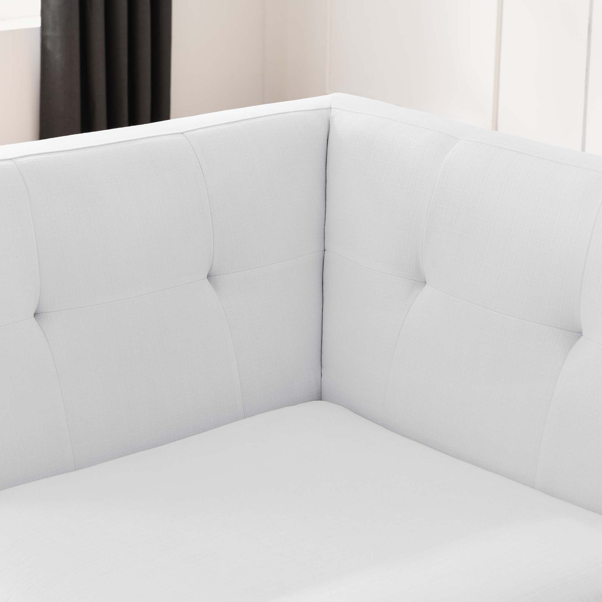 White fabric corner chair with tufted back cushions in a bright living room.