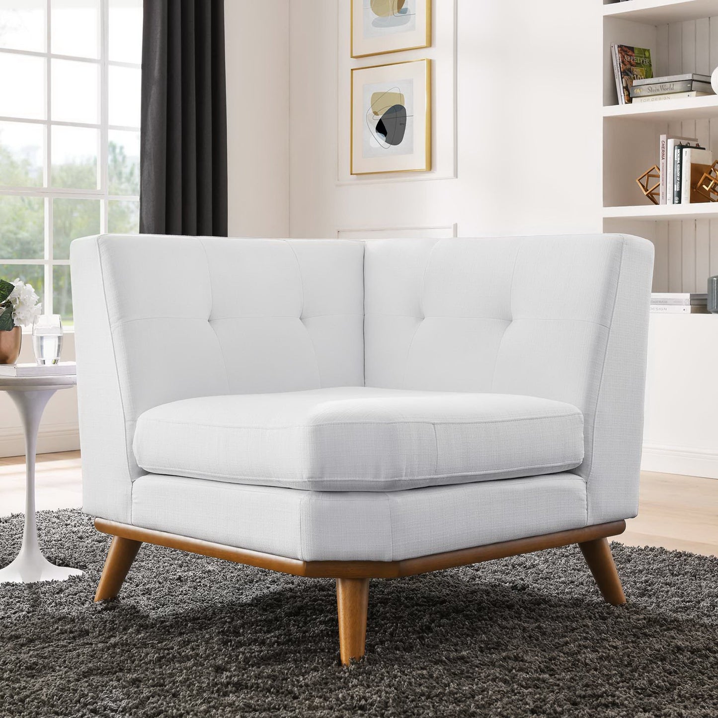 White fabric tufted mid-century corner chair with wooden tapered legs in a bright living room.