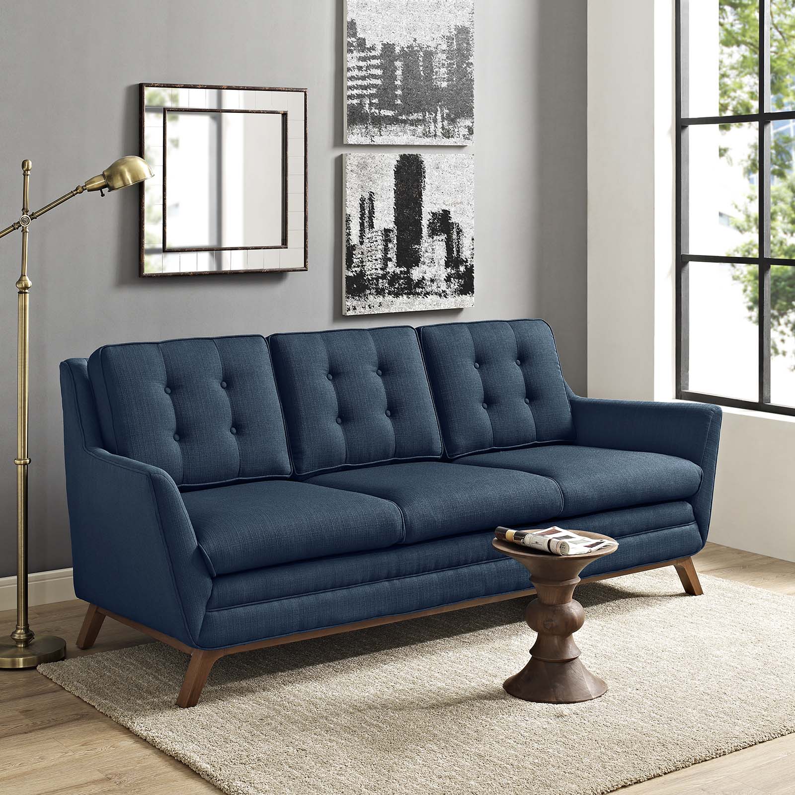 Azure blue tufted fabric sofa with wooden legs in a modern mid-century living room, beige rug, round wood coffee table.