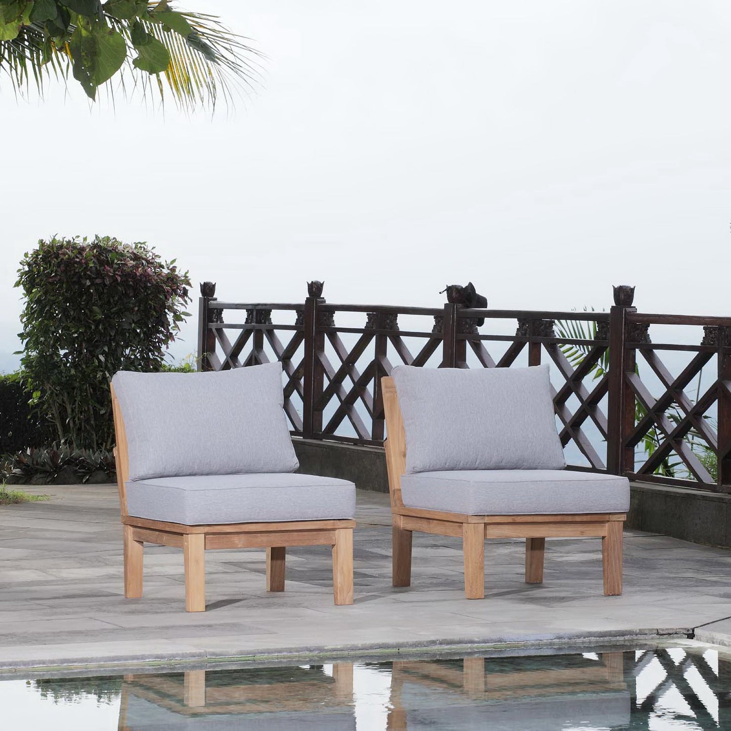 Two wooden-frame outdoor chairs with light gray cushions on a stone patio by a wooden railing.
