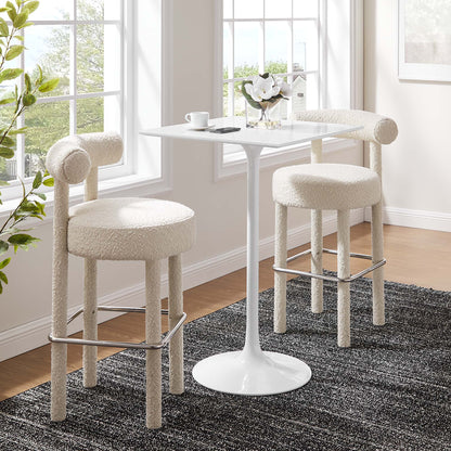 White tulip pedestal table with two boucle upholstered bar stools and chrome foot rails in a sunlit breakfast nook.
