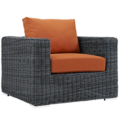 gray woven outdoor armchair with burnt orange cushions; boxy frame and sturdy wicker construction.