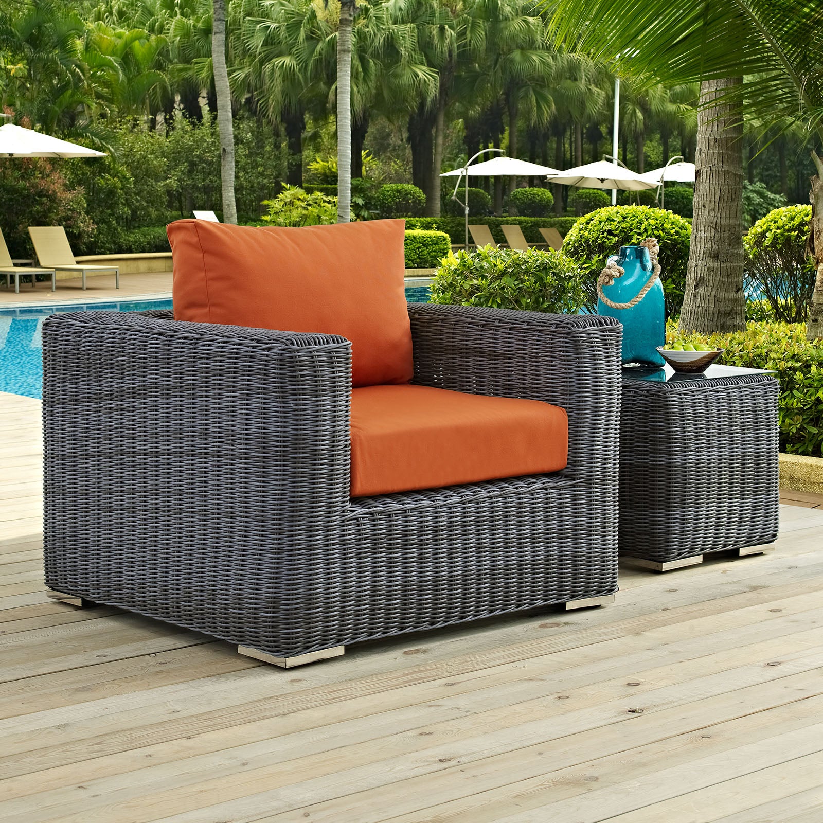 Gray fabric outdoor armchair with orange cushions and a matching side table beside a pool.