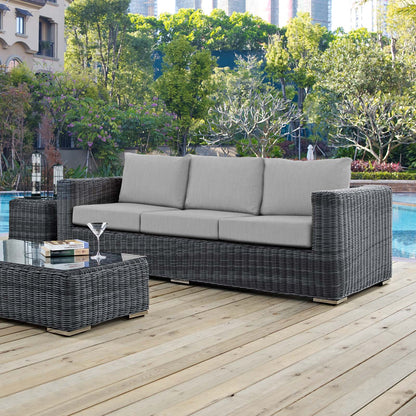 Grey wicker outdoor 3-seat sofa with light grey cushions and matching glass-topped coffee table by pool on wooden deck.