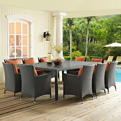Outdoor dining table on a wooden deck beside a pool, with dark gray chairs and orange cushions around a rectangular table.