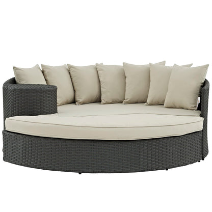 Round outdoor wicker daybed in dark charcoal with beige cushions and beige pillows.
