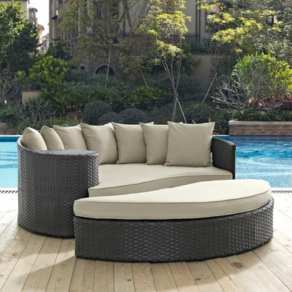Round dark wicker outdoor daybed with light beige cushions, modular curved sections and backrest pillows by pool.